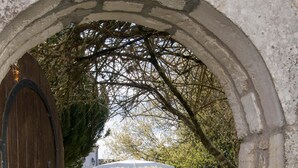 An arched stone doorway leading to a courtyard with a white umbrella, red chairs, and a stone table. - Villa PIERROT      . (La Flotte)