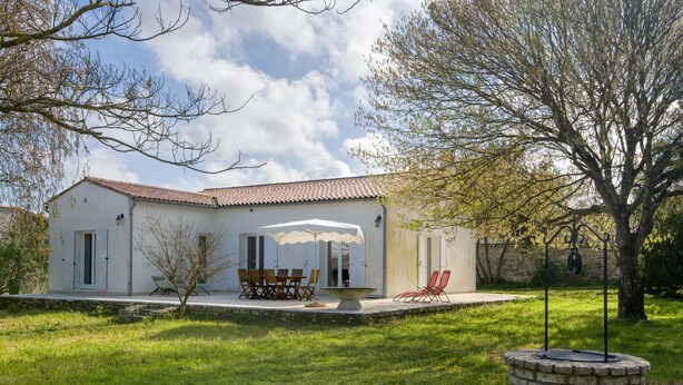 A white building with a tiled roof, a patio with outdoor furniture, and a stone well. - Villa PIERROT      . (La Flotte)