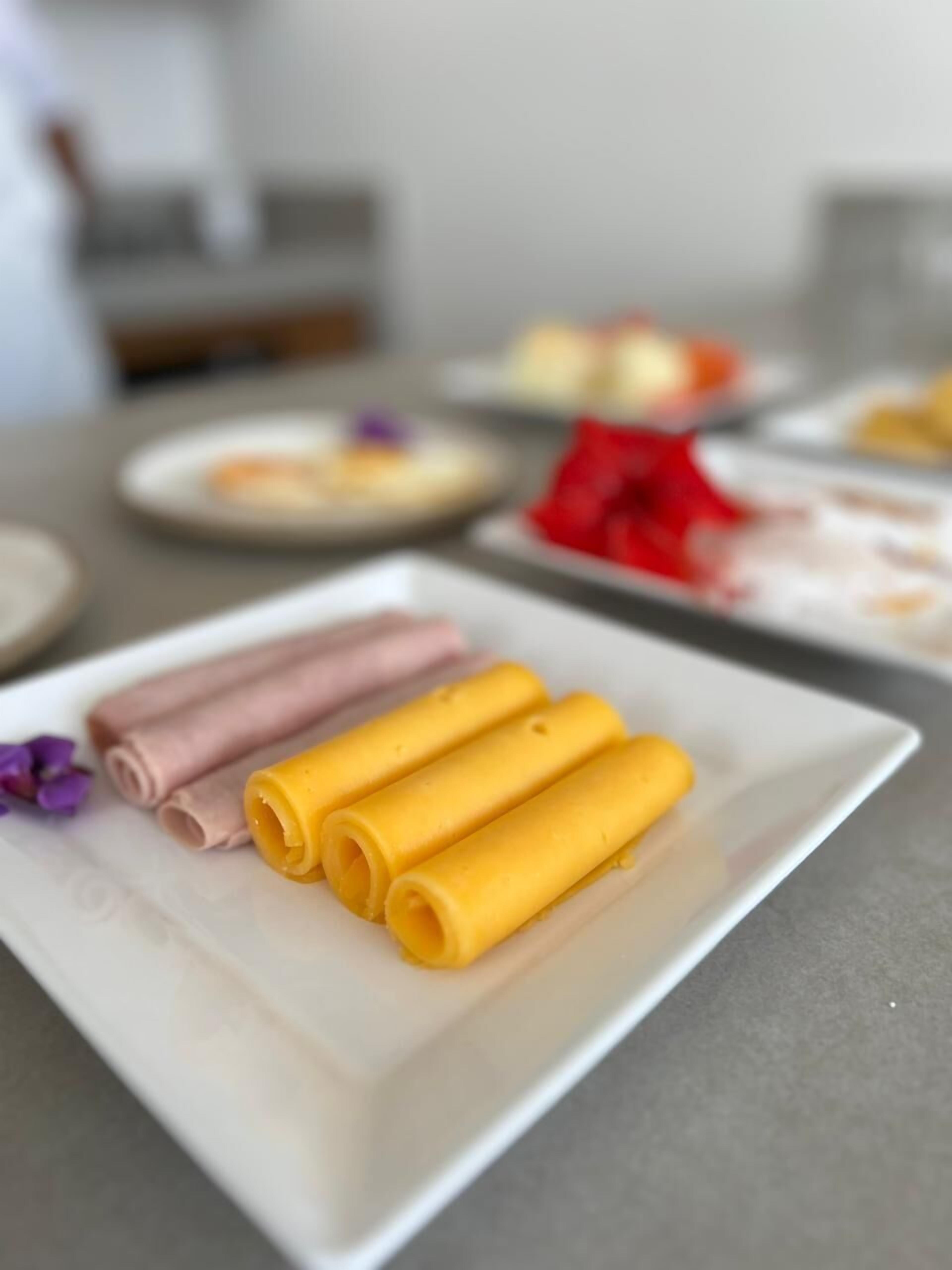 Um prato branco com três rolinhos em tons de rosa, amarelo e branco.