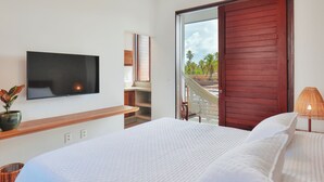 A modern bedroom with a large bed, a flat-screen TV mounted on the wall, and a view of the outdoors through a sliding door. - Pousada Praia do Patacho (Porto de Pedras)