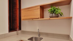 A compact kitchen with a built-in sink, wooden cabinets, and a small refrigerator. - Pousada Praia do Patacho (Porto de Pedras)