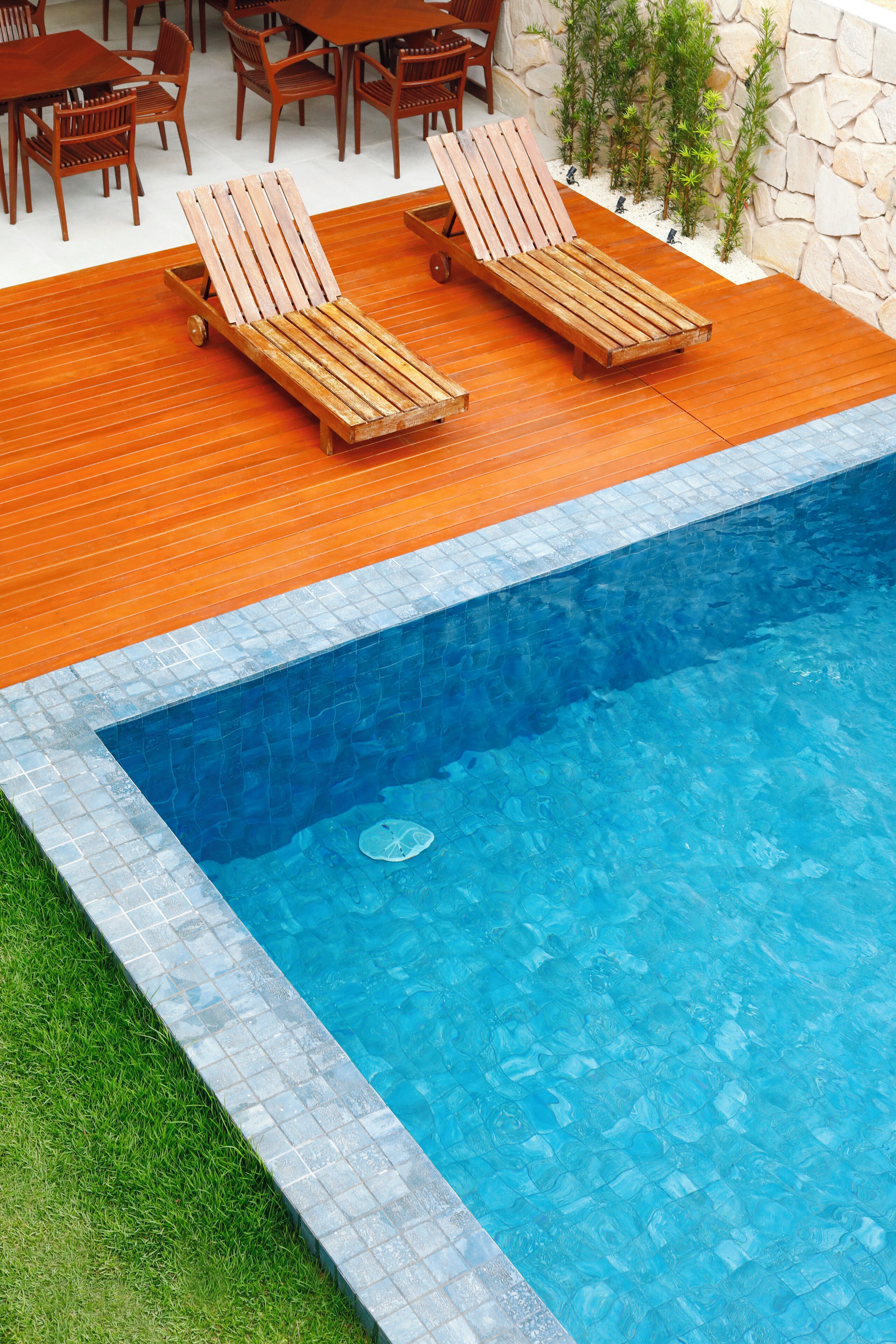 A pool area with wooden loungers, a stone wall, and a tiled deck.