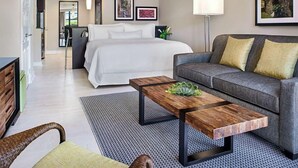 A modern hotel room with a bed, a grey sofa, a wooden coffee table, and a small side table. - Luxury resort with beach, pool, many amenities (Cruz Bay)