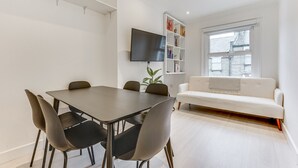 En moderne stue med spisebord, stole, sofa, fjernsyn og reol.