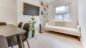 En moderne stue med en hvid sofa, et fladskærms-tv ophængt på væggen, en reol og en potteplante.