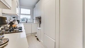 Et moderne køkken med hvide skabe, en gasovn og et vindue med naturligt lys.
