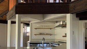 A modern kitchen with a central island, wooden beams, and a view to an upper level. - RustRidge House, two bedroom two bath home (St Helena)