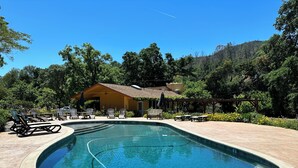 A swimming pool with lounge chairs and a yellow building in the background. - RustRidge House, two bedroom two bath home (St Helena)