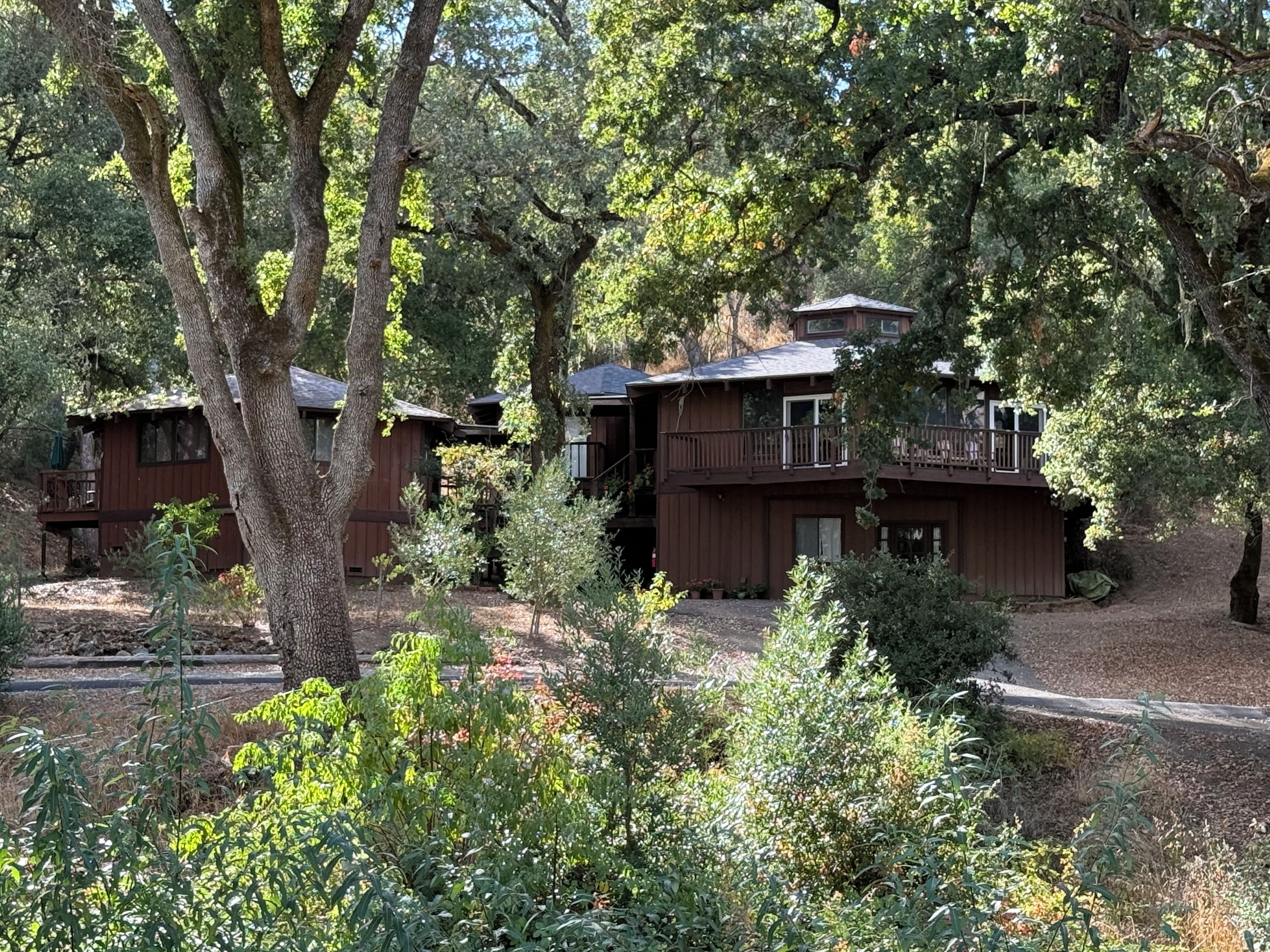 A cabin with a deck and a covered porch, surrounded by trees.