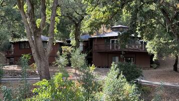 A cabin with a deck and a covered porch, surrounded by trees.