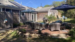 Un patio con mobiliario exterior, una parrilla y un área cubierta con una sombrilla.