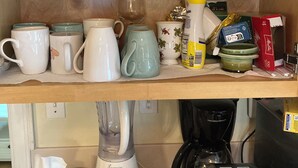 Una repisa de cocina con distintos vasos, tazas de cerámica y una cafetera.