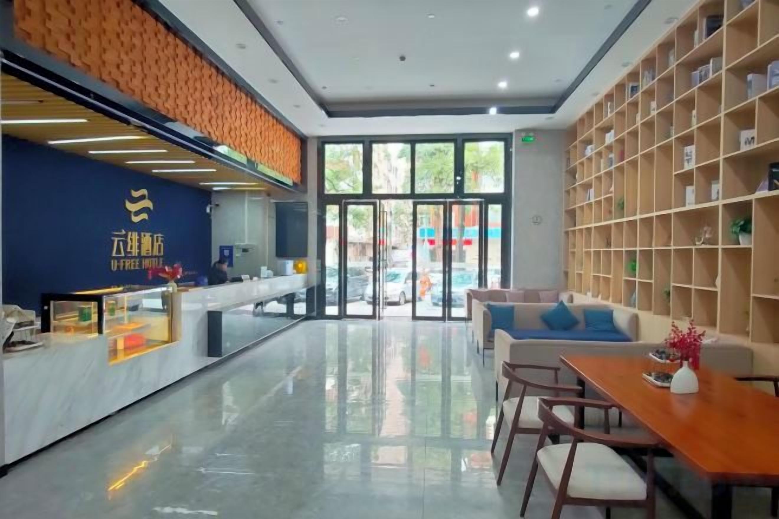 A hotel lobby with a reception desk, seating area, and a bookshelf.