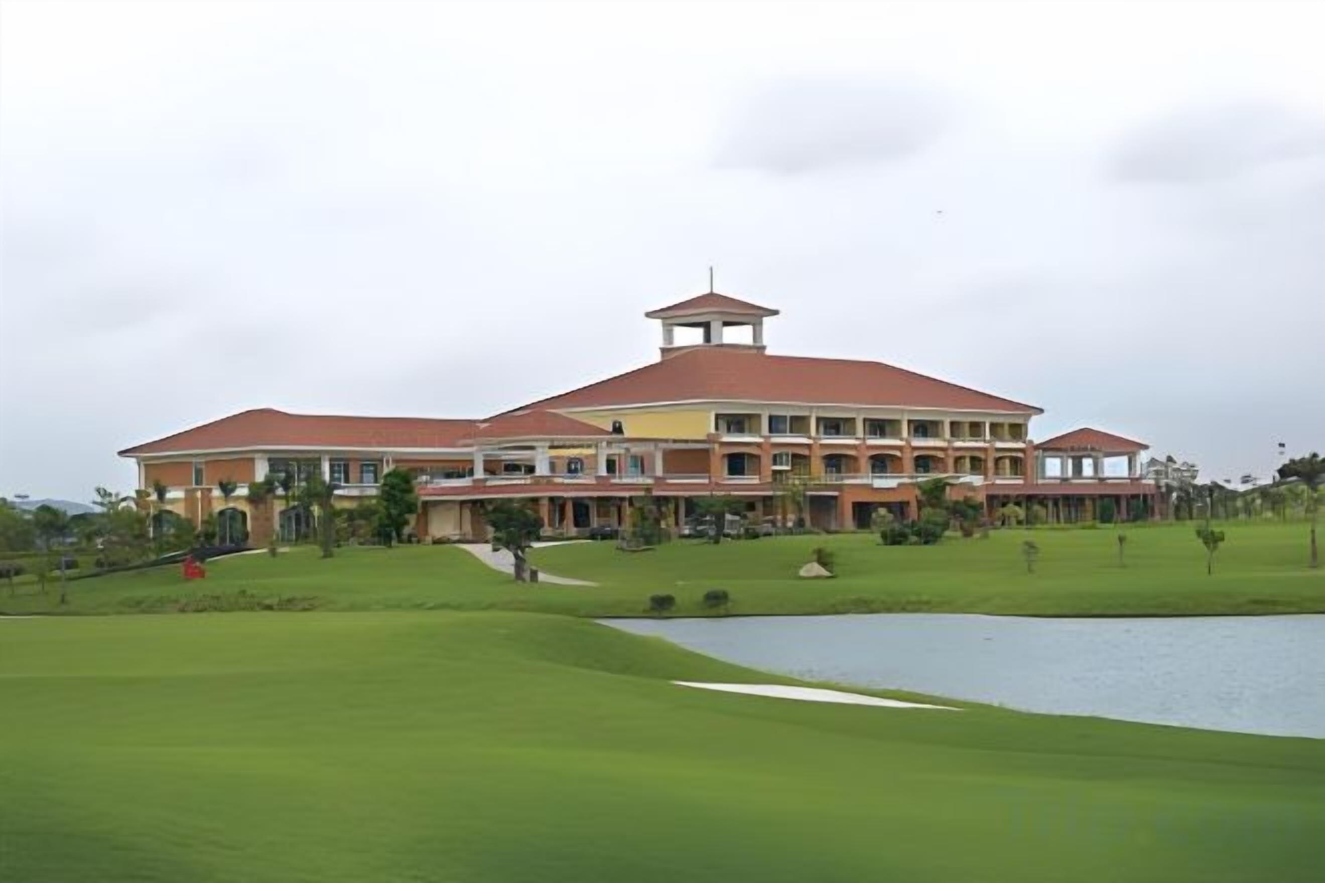A large building with a red roof and multiple floors, surrounded by a well-maintained lawn and a body of water.