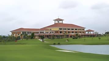A large building with a red roof and multiple floors, surrounded by a well-maintained lawn and a body of water.