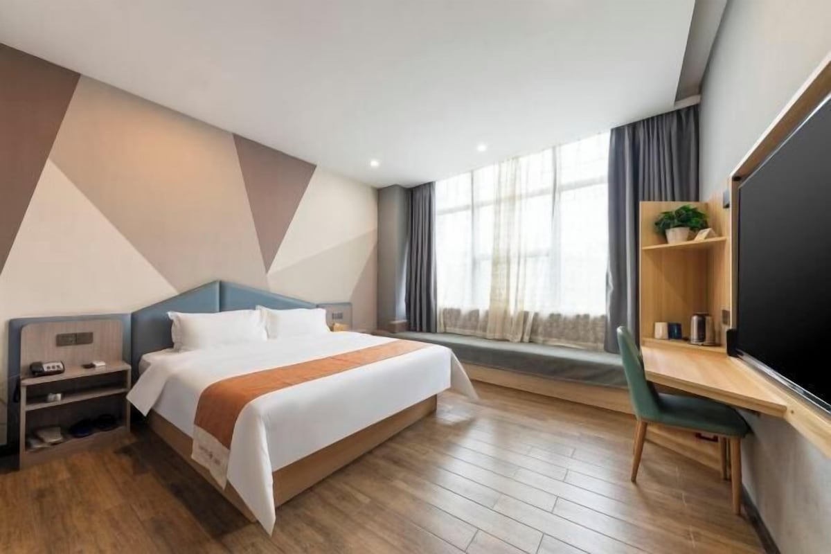 Ein modernes Hotelzimmer mit einem großen Bett, einem Schreibtisch und einem Fenster mit Vorhängen.