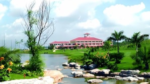 A large building with a red roof, surrounded by a well-maintained lawn, a small pond, and various plants. - U-FREE Hotel (Dongguan Xiegang Square) (Dongguan)