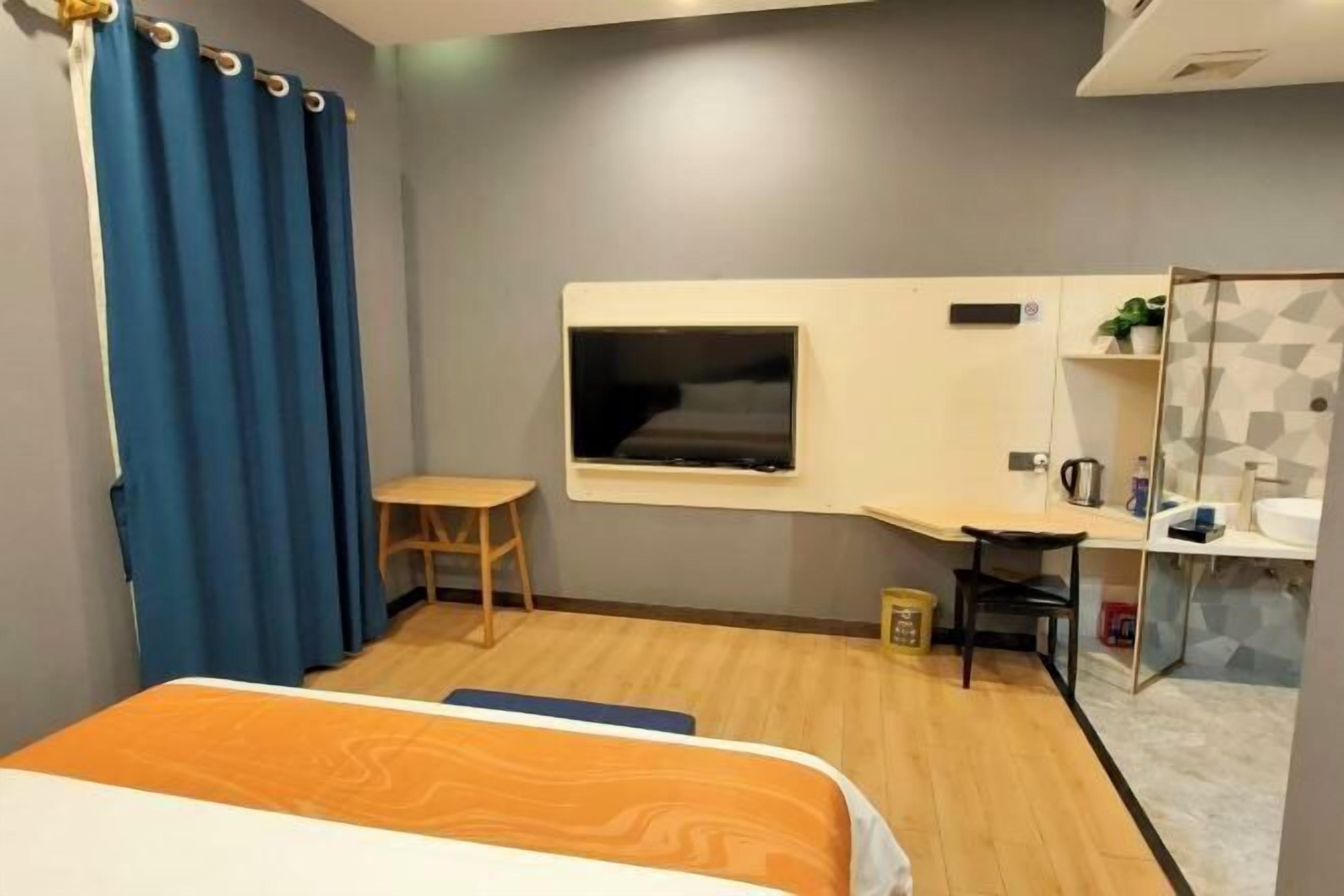 Hotelkamer met een bed, bureau, stoel, televisie, spiegel en een kleine badkamerruimte.