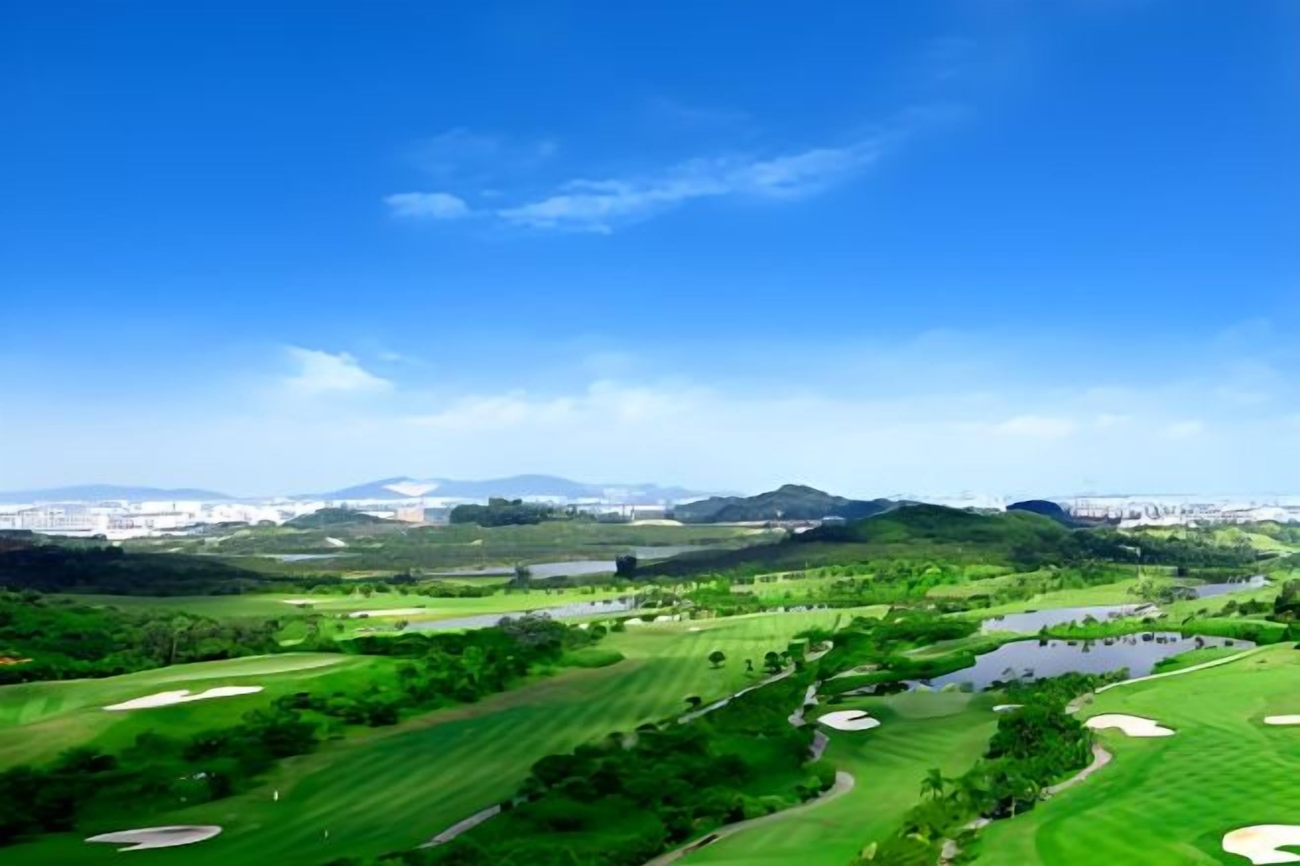 A golf course with a water body, green areas, and distant buildings.