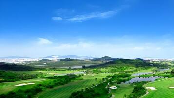 A golf course with a water body, green areas, and distant buildings.