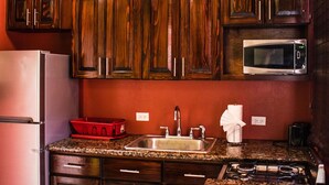 Una cocina con armarios de madera oscura, encimera de granito, pileta de acero inoxidable, microondas y dos lámparas colgantes.