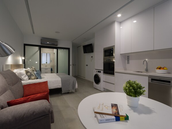 Un ambiente living moderno e funzionale, con un letto, un divano, un tavolo da pranzo, una lavatrice, un forno e un lavandino.