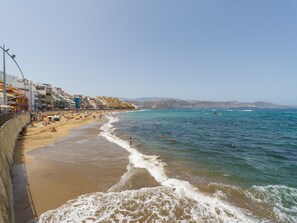 Una spiaggia con una passeggiata fiancheggiata da edifici colorati, una riva sabbiosa e il mare.