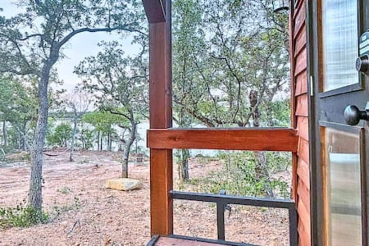 Une structure en bois dotée d’une porte en métal, entourée d’arbres et bordée d’un paysage aride.
