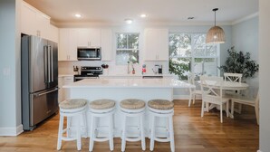 A modern kitchen with white cabinets, a stainless steel refrigerator, a microwave, and a large island with bar stools. - Coastal Quarters dog friendly, 4 bedroom home in Old Town Bluffton (Bluffton)