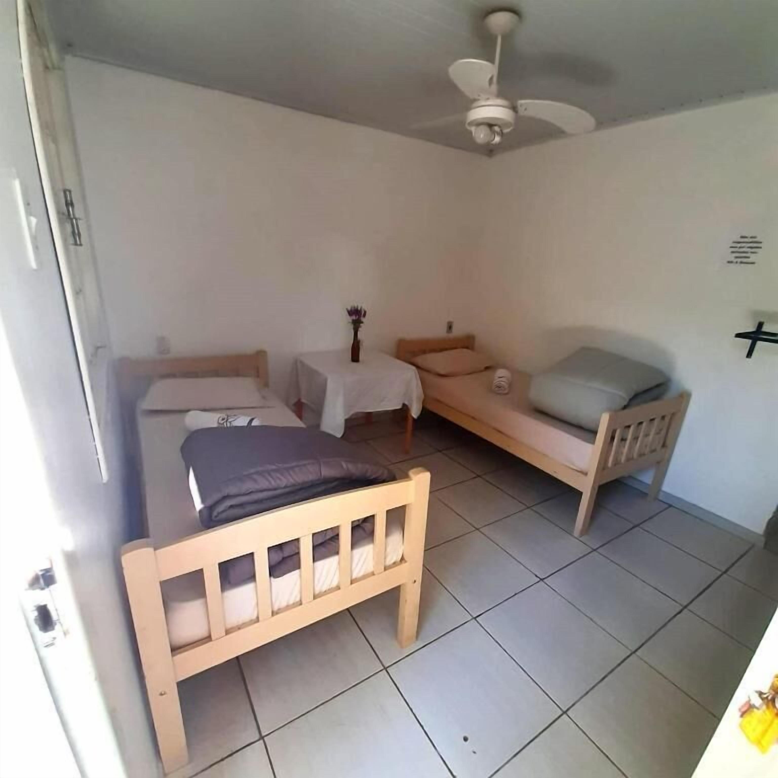 Une chambre à coucher avec un lit, une petite table sur laquelle est posé un vase, et un ventilateur de plafond.