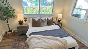 Une chambre à coucher avec un grand lit, deux tables de chevet, une fenêtre donnant sur un paysage verdoyant et un luminaire au plafond.