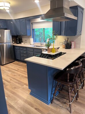 A modern kitchen with dark blue cabinets, a stainless steel refrigerator, a gas stove, and a large island with bar stools.