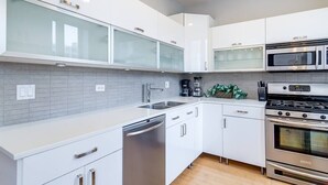 Een moderne keuken met witte kasten, een roestvrijstalen vaatwasser, een dubbele oven en een magnetron.