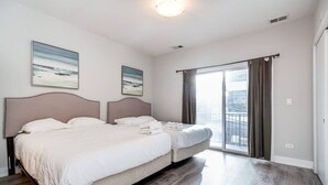 Een moderne hotelkamer met een groot bed, een tweede kleiner bed, een balkon met gordijnen en twee schilderijen aan de muur.