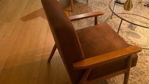 Een moderne woonkamer met een houten bankje, twee bruine leren fauteuils, een glazen salontafel en een tapijt met een patroon.