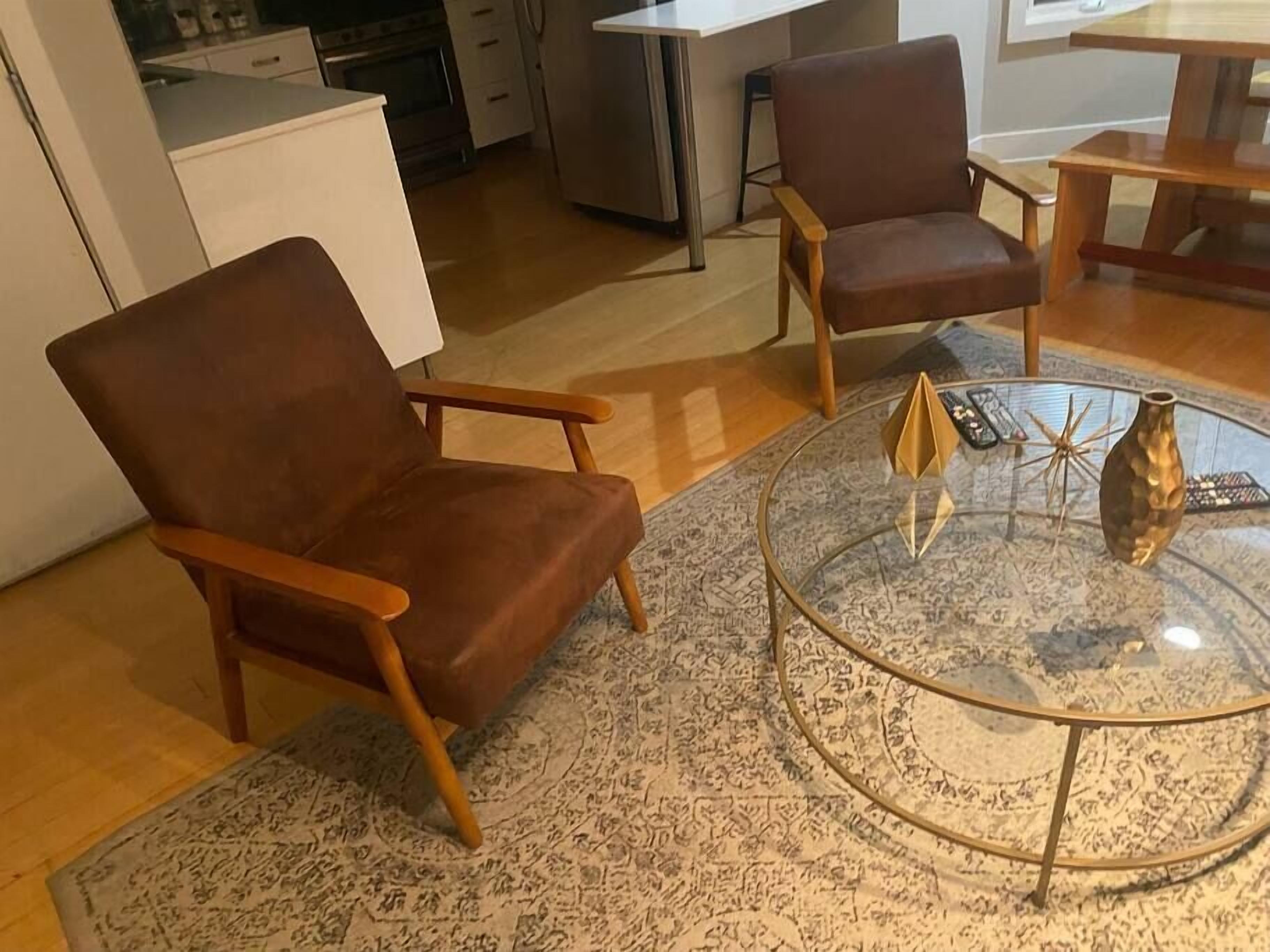 A living room with two brown leather armchairs, a glass coffee table with decorative items, and a patterned rug.