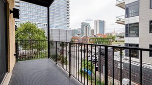 Een balkon met een metalen hekwerk, uitzicht op een stadslandschap en een verhard vloer.