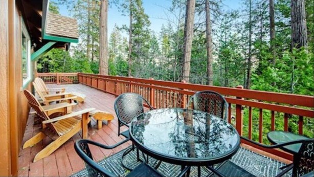 A wooden deck with outdoor furniture, surrounded by tall trees.