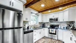 A modern kitchen with stainless steel appliances, white cabinetry, and a wooden ceiling.