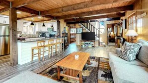 A spacious living area with a wooden ceiling, a sofa, a coffee table, and a kitchen area with a bar and seating.