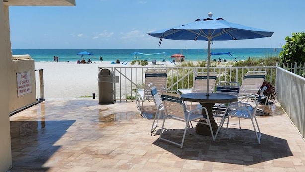 Un patio con una mesa y sillas, una sombrilla azul y vista a la playa.