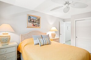 A bedroom with a bed, two bedside tables, a ceiling fan, a framed picture on the wall, and a door.