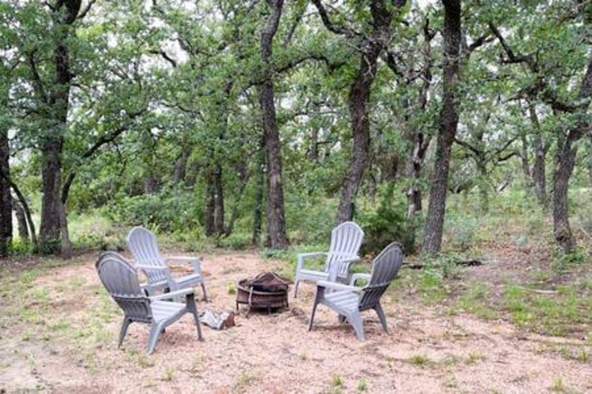Zona boscosa con dos sillas Adirondack y un pequeño hogar para fuego.