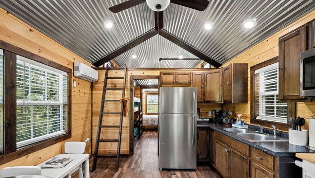 A compact kitchen with wooden cabinets, a stainless steel refrigerator, and a window with blinds. - 6 Tiny Town Hico - Big Texas Ranch Experience (Hico)