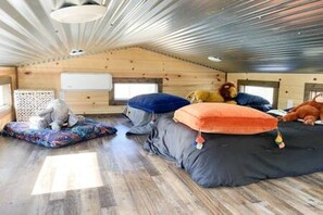 A cozy room with a sloped ceiling, a bed with colorful pillows, and a small white dog. - 6 Tiny Town + Monthly + Utilities + Comfy Stay (Hico)