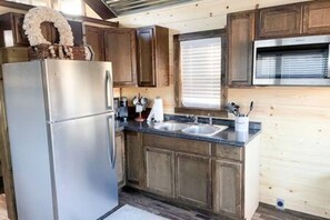 A kitchen with wooden cabinets, a stainless steel refrigerator, a double sink, and a window with blinds. - 6 Tiny Town + Monthly + Utilities + Comfy Stay (Hico)