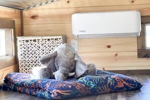 A room with a wooden interior, an air conditioning unit, a patterned cushion, and a colorful blanket. - 6 Tiny Town + Monthly + Utilities + Comfy Stay (Hico)
