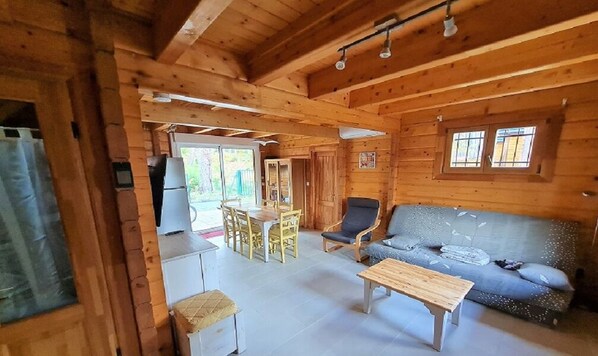 A wooden cabin interior with a dining area, a sofa, and a table.
