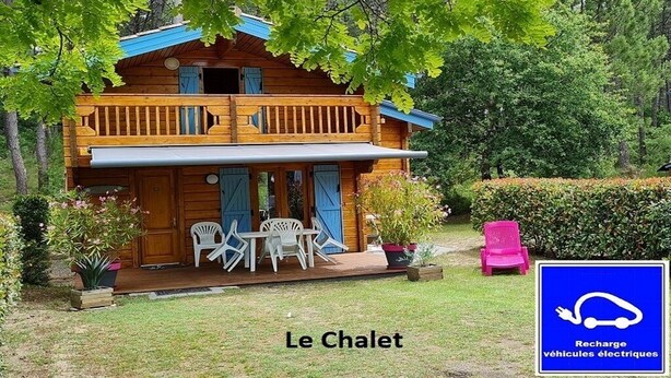 A wooden cabin with a balcony, outdoor seating, and a sign indicating electric vehicle charging.