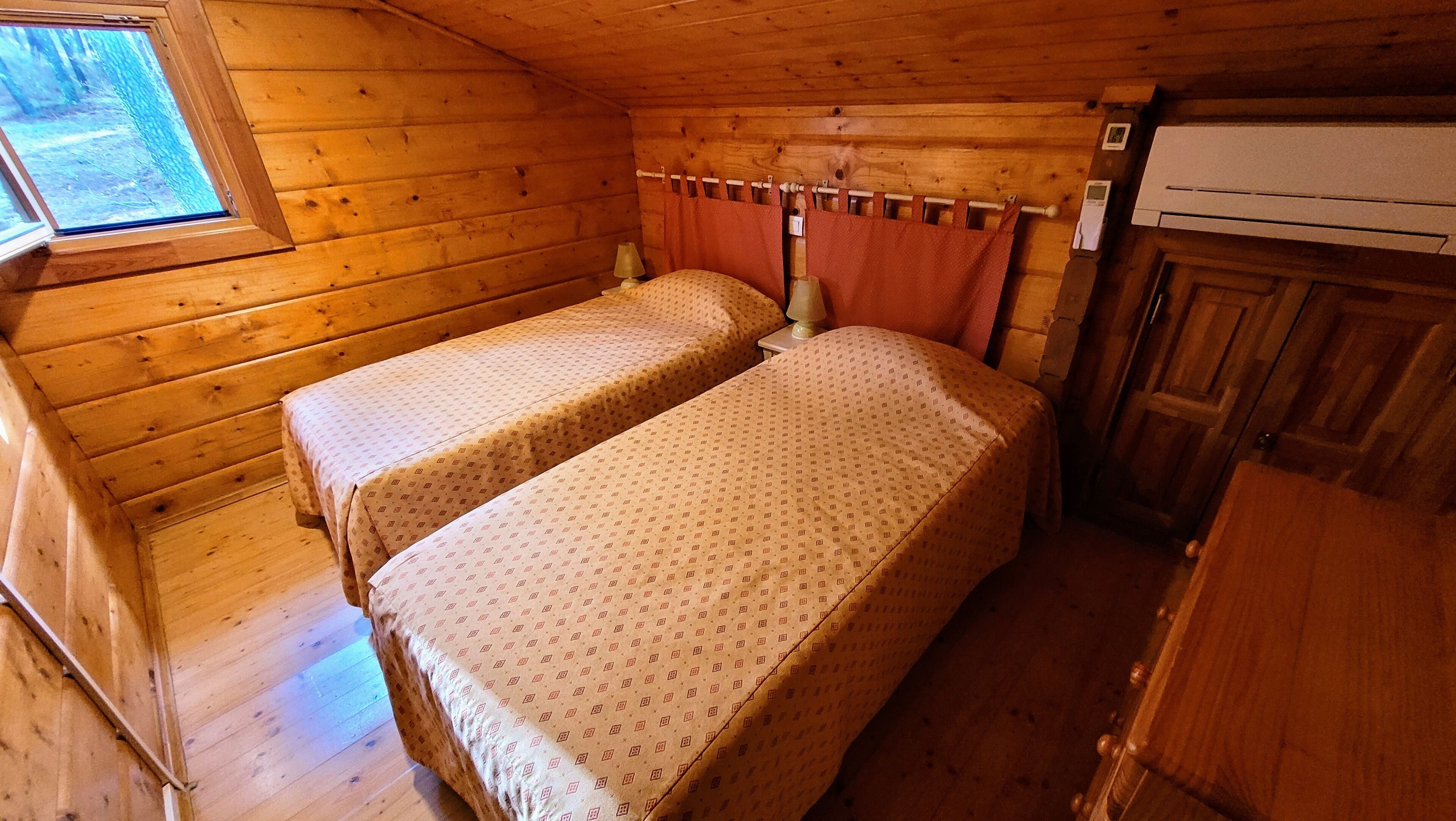 Une petite chambre de cabane accueillante, avec deux lits, une fenêtre et un intérieur en bois.